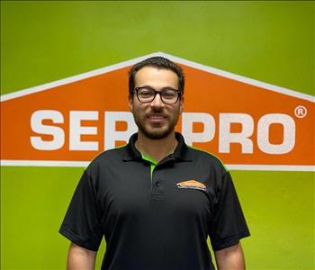 Brown haired male with glasses standing in front of a SERVPRO green background with a SERVPRO logo on the wall. 