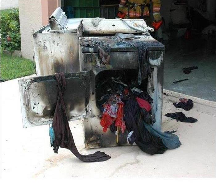 Dryer on fire with clothes hanging out of it